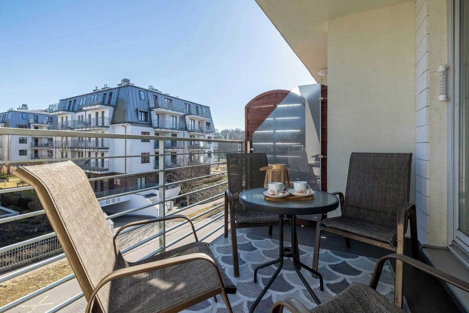 A balcony with two chairs and a small table provides a comfortable outdoor seating area. Nearby buildings and rooftops can be seen in the background.