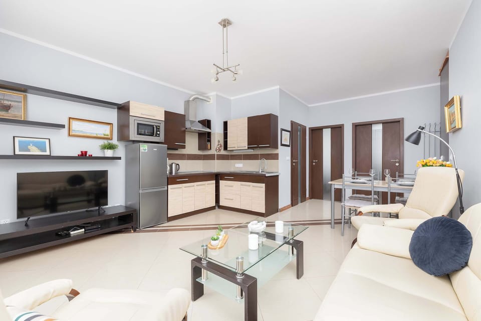  A spacious, well-lit living room with a dining area in the background, offering a cozy sofa and decorative elements. The neutral tones create a warm and inviting ambiance.