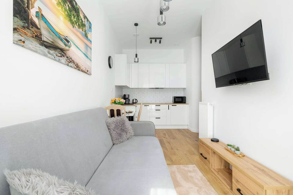 A different angle of the living room highlighting a mounted TV, gray sofa, and partial view into the kitchen area.