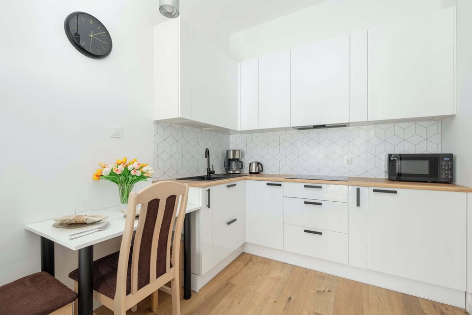 An open-plan living area with a dining table set for two, leading into a white modern kitchen.
