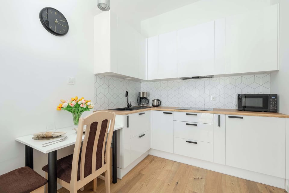 An open-plan living area with a dining table set for two, leading into a white modern kitchen.
