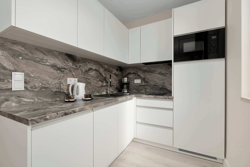 A kitchen with white cabinetry, built-in appliances, and a sleek countertop with a marble-style finish.