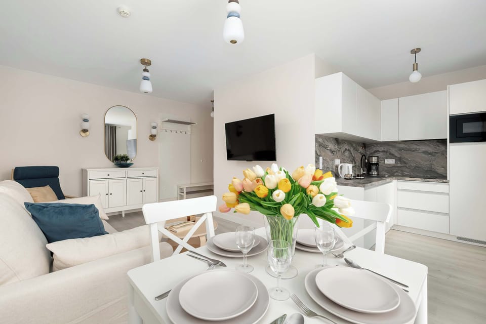 A dining table set with plates and flowers, with the kitchen area visible in the background.