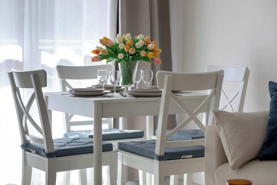 A dining setup with a white table, matching chairs, and a vase of colorful flowers placed in the center.