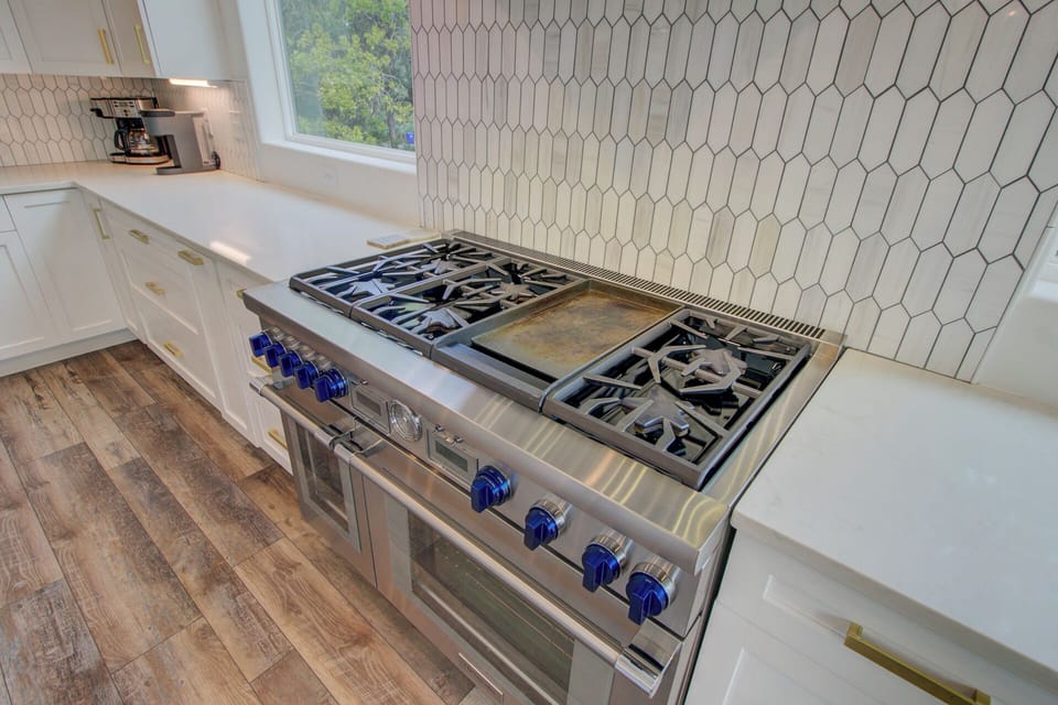 Your gourmet kitchen features a professional gas range with blue knobs and elegant white geometric backsplash.
