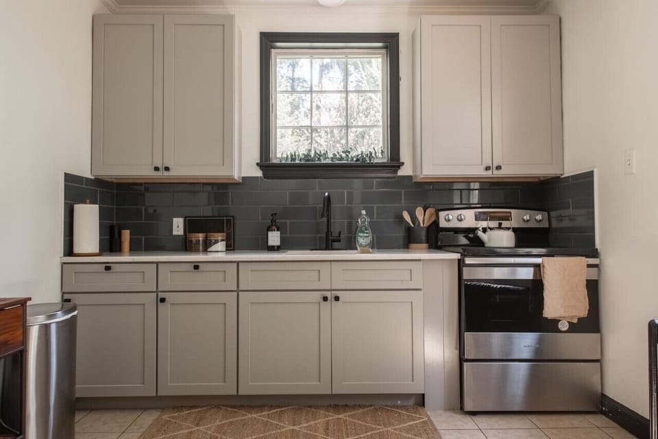 Kitchen with cabinets a window above the sink, a stove, and black tile backsplash