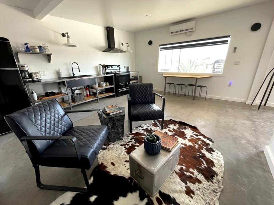 Open-plan living area with cowhide rug, leather sofa, and industrial kitchen beyond