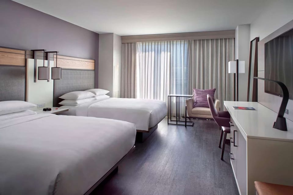 Room with two queen beds, desk, and lounge chair by the window