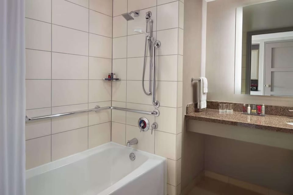 Tile bathroom with tub, grab bars, and lighted vanity mirror
