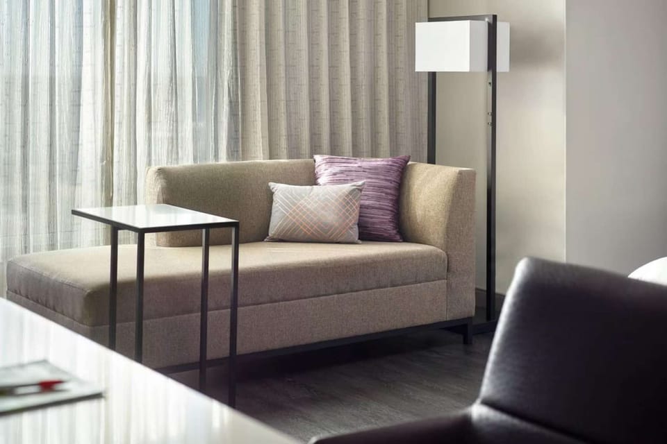 Small sofa with pillows and floor lamp near window drapes