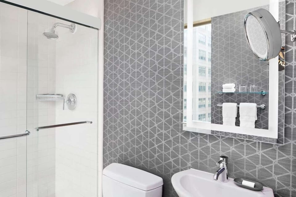 Bathroom with glass shower, lit mirror, and patterned gray walls