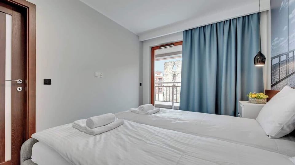 Another bedroom view with a large bed, warm wooden tones, and expansive windows offering plenty of natural light. Blue curtains add a touch of elegance.