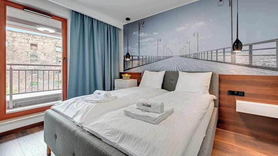 A cozy bedroom with a large bed and minimalist decor. The wall behind the bed features a beautiful black-and-white cityscape mural.