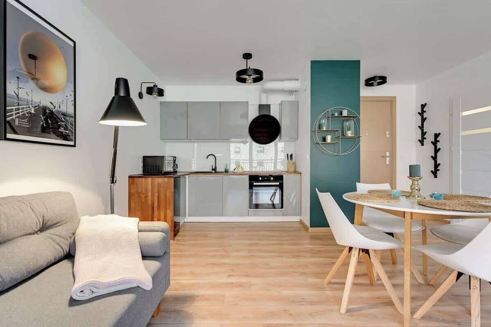 A spacious living room with a gray sofa, a coffee table, and a dining area with modern chairs, enhanced by large windows for natural light.