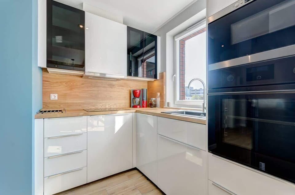 A modern kitchenette in light colors with wooden accents and contrasting black elements, creates an elegant and functional space ideal for preparing meals.