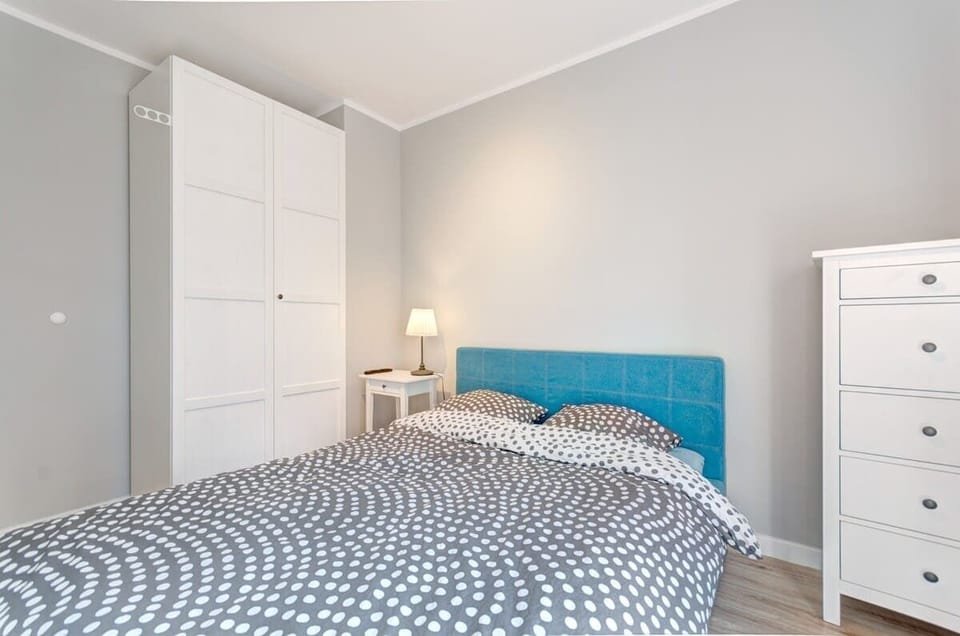 The bedroom impresses with subtle elegance, combining neutral gray walls with a distinctive turquoise bed headboard. Complemented with white furniture and delicate accessories, it creates a pleasant, harmonious space.