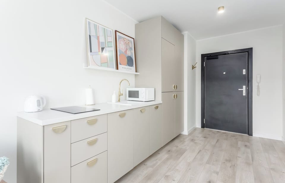 A small kitchenette with a microwave, sink, and storage cabinets. The hallway leads to the rest of the apartment.