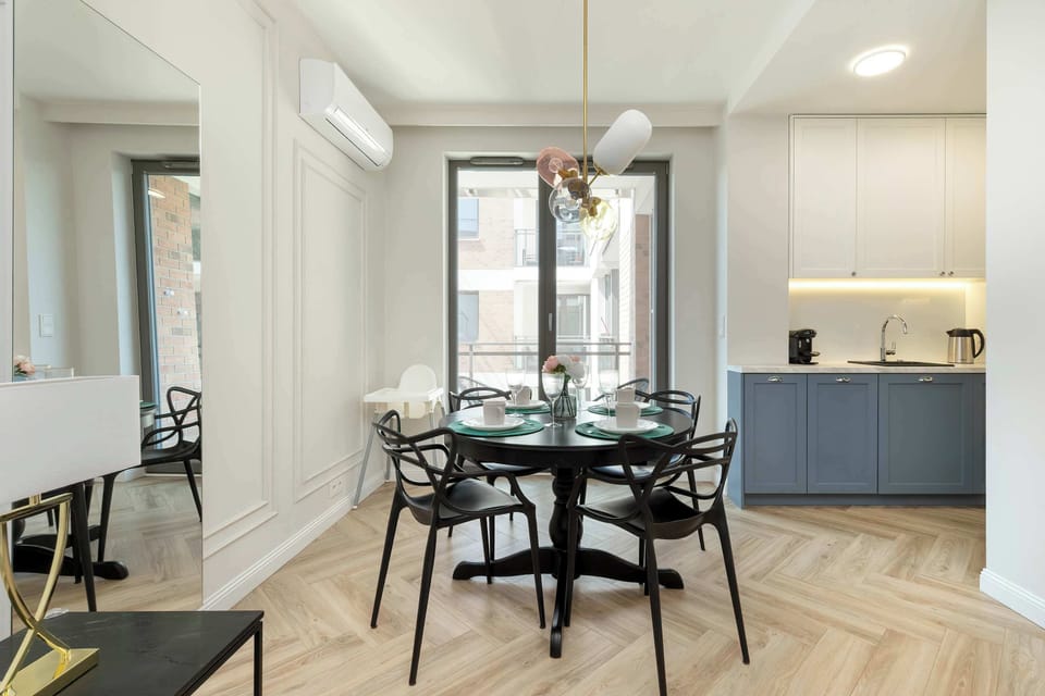 A chic living room area with elegant furniture and floor-to-ceiling windows. The dining table is conveniently placed near the balcony entrance.