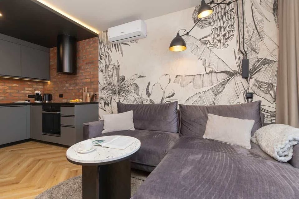 A combined living and kitchen area with a wall mural, dark sofa, and circular tables.

