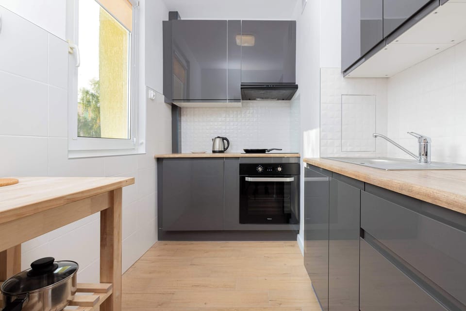 A small but functional kitchen with white cabinetry and stainless steel appliances. A wooden shelf holds neatly organized pots and pans.