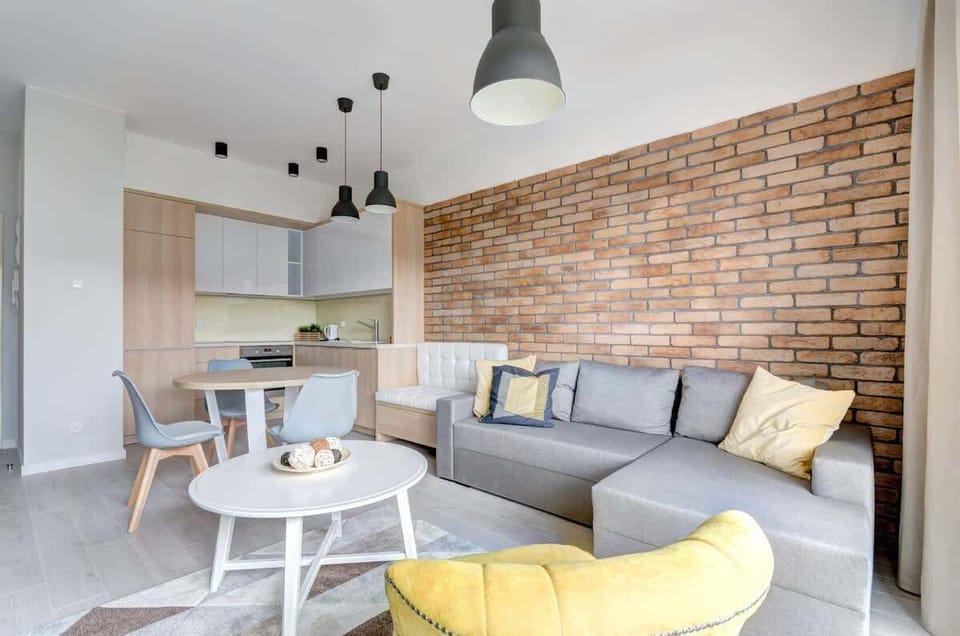 The living room is stylishly decorated with a brick accent wall, comfortable seating, and a modern kitchen area with a dining table and pendant lights.