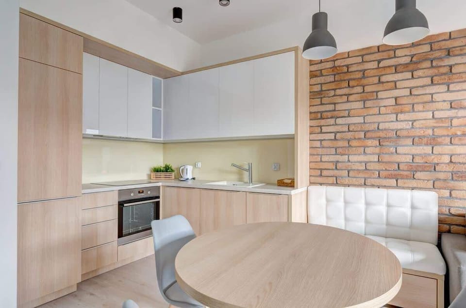 The kitchen features light wood cabinets with a white countertop, complemented by a cozy dining nook with a brick accent wall.