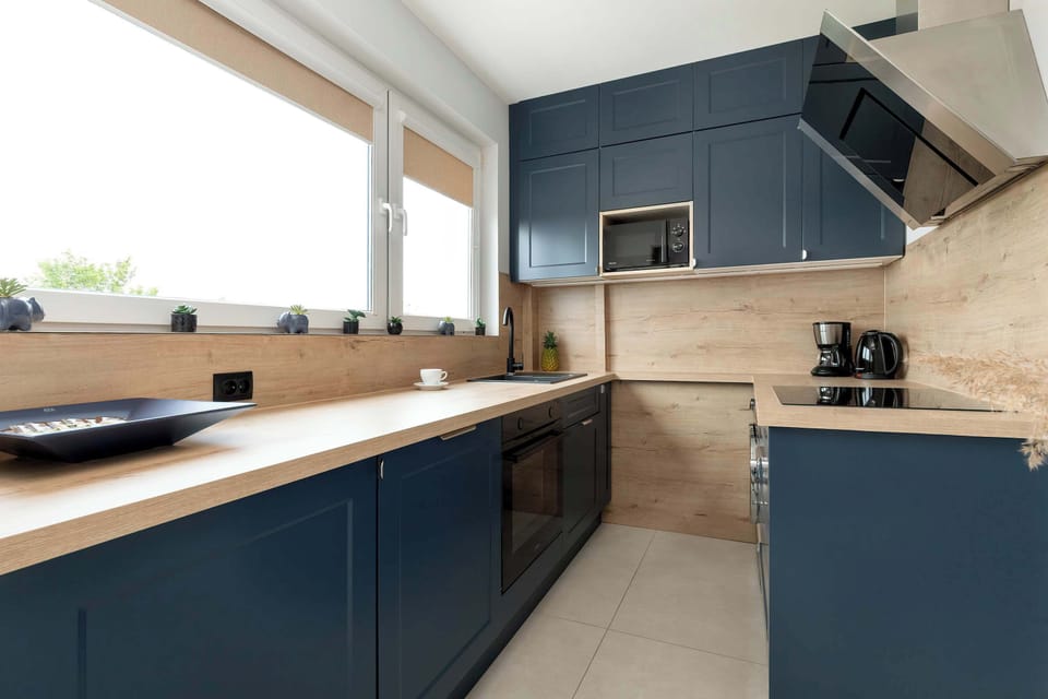A modern kitchen with navy blue cabinets, wooden countertops, and built-in appliances.