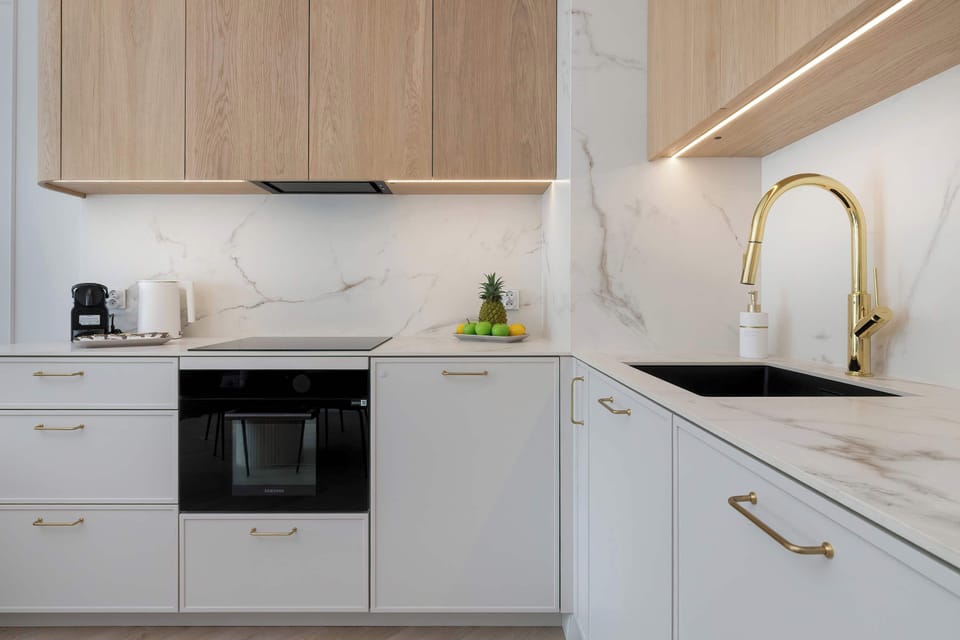Compact L-shaped kitchen with white cabinetry, wooden accents, and built-in appliances.