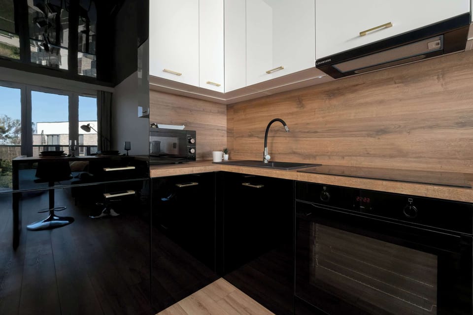 A corner view of the kitchen with black lower cabinets and wood countertops under white upper cupboards.