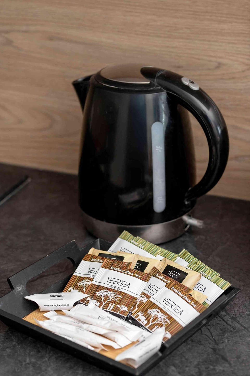 A close-up of a black electric kettle and an assortment of coffee and tea supplies neatly placed on a tray.