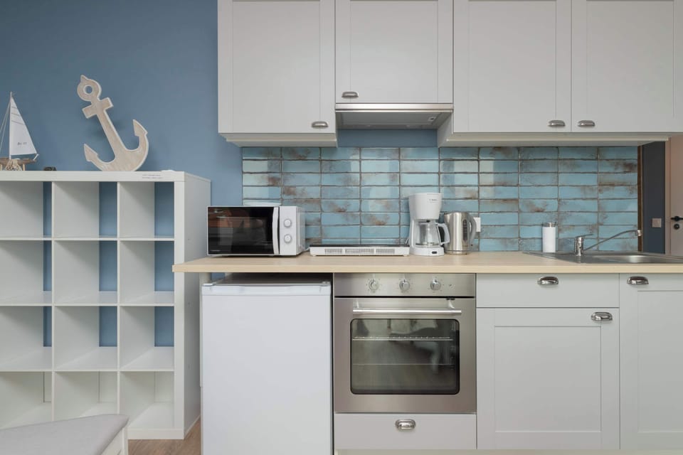 A fully equipped kitchen featuring white cabinetry and blue tile backsplash. It includes modern appliances like an oven, microwave, and coffee maker.