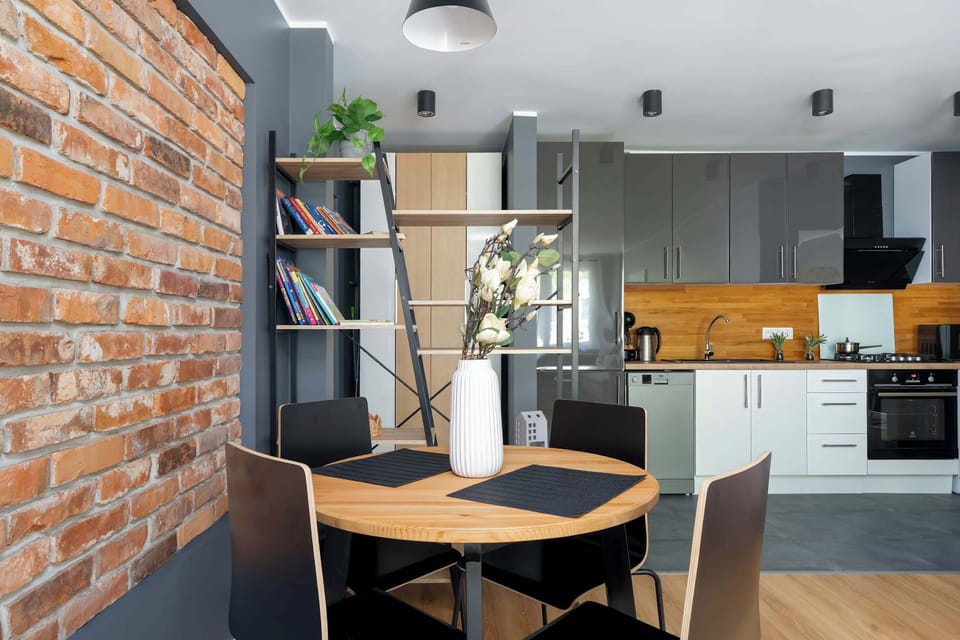A close-up of a dining area table against a textured red brick wall, with a vase of white flowers and minimal décor.