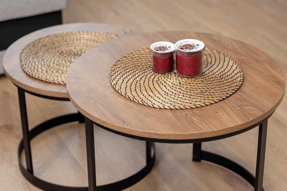 A close-up of two round woven coffee tables with red decorative candles on top. The tables add a natural touch to the living area.