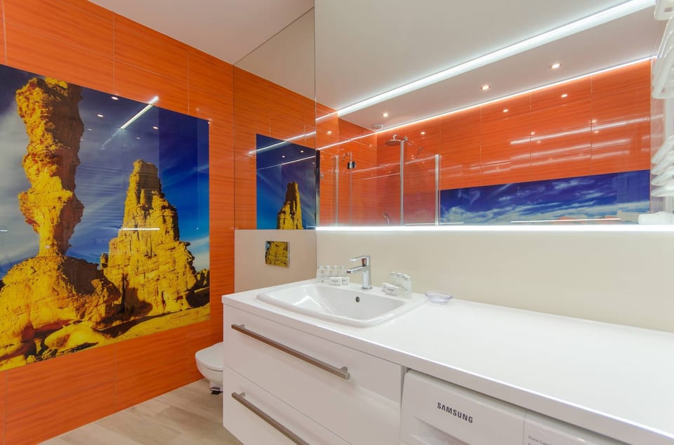 A modern bathroom with an orange accent wall, a wide mirror, and a clean aesthetic.