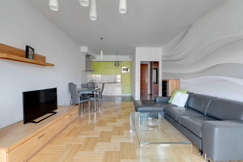 A contemporary living area with a gray L-shaped sofa set against a textured, wave-patterned wall. The minimalist decor highlights the room's modern design aesthetic.
