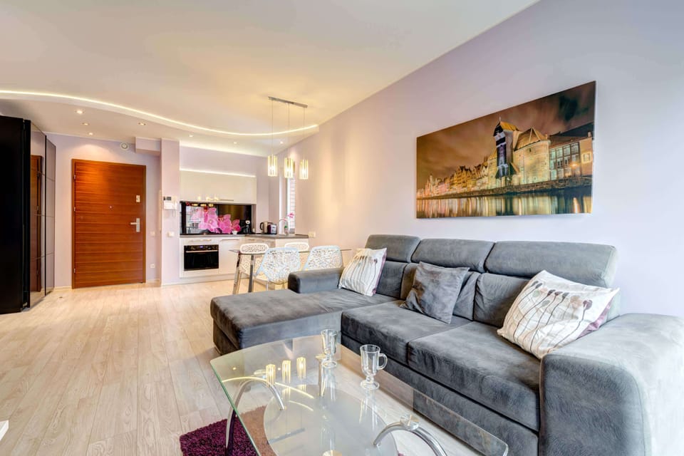 Modern and bright living room with a sofa bed, TV and kitchenette with dining area.
