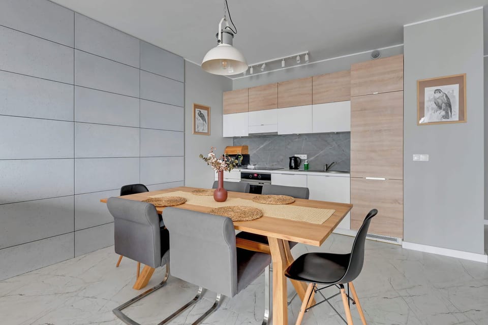 A modern kitchen open to the living room combines functionality with aesthetics. Furniture in shades of white and light wood harmoniously complements the marble floor, creating a space full of class and order.