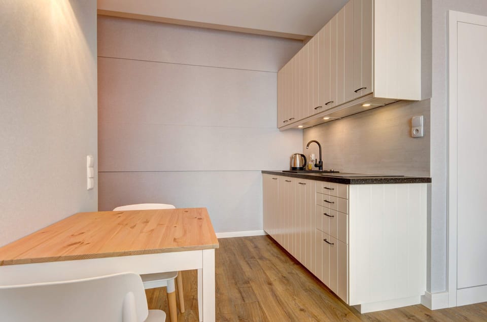 A modern kitchenette with sleek white cabinets, wooden countertops, and a dining area perfect for meals or work.