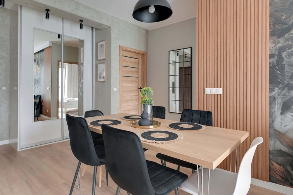 A cozy yet modern open-plan living space with a wooden dining table and stylish chairs. A combination of warm wood accents and sleek furnishings creates an inviting ambiance.