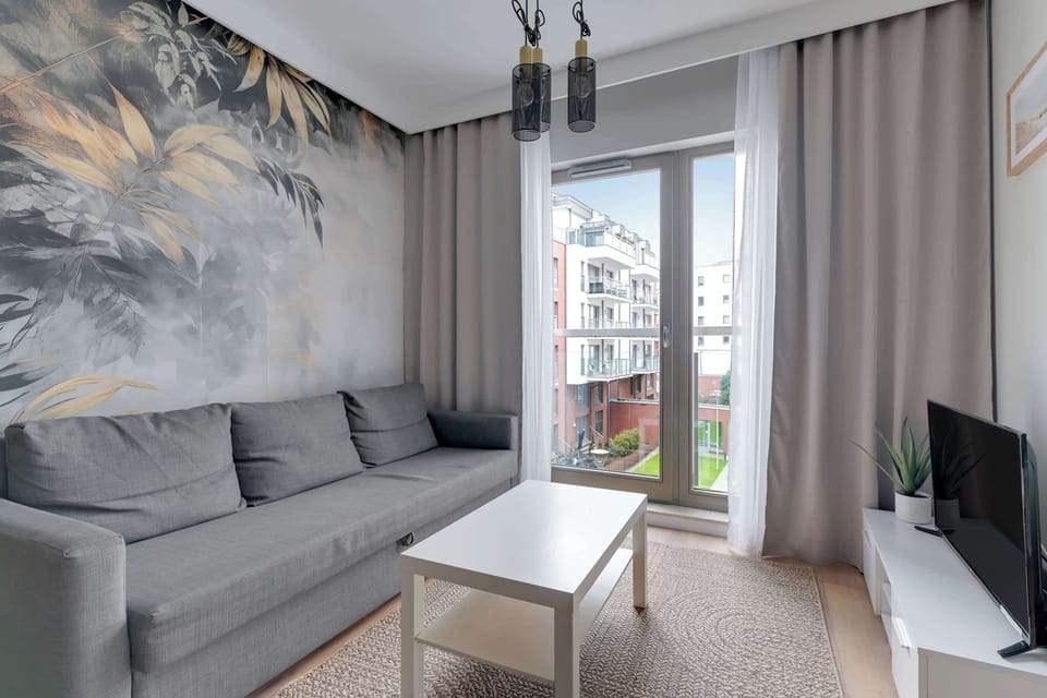 A living room with a gray sofa, a coffee table, and an artistic mural on the feature wall. Natural light from the large window highlights the elegant decor.