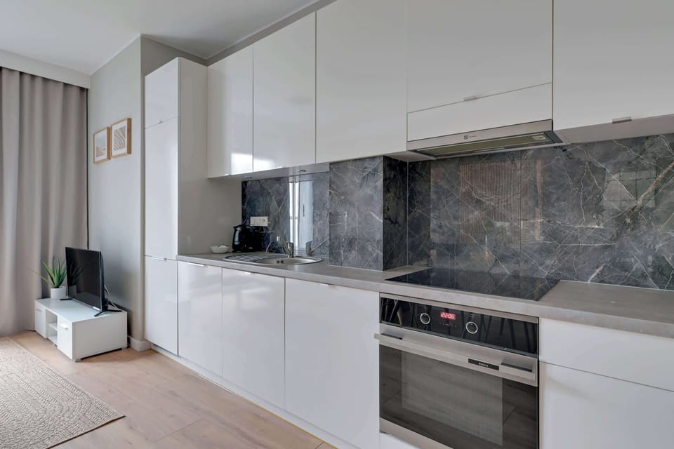 A sleek, minimalist kitchen with white cabinetry and a marble backsplash. The integrated appliances and clean lines create a high-end, modern aesthetic.