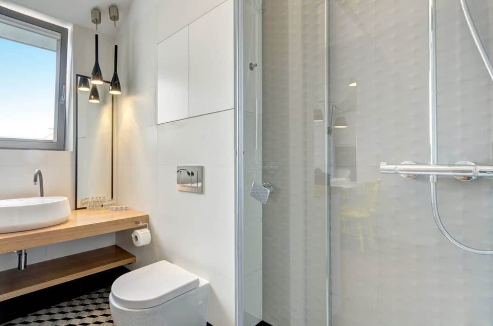 The bathroom is a combination of simplicity, style and functionality. There is a shower, a sink, a toilet and a mirror. 