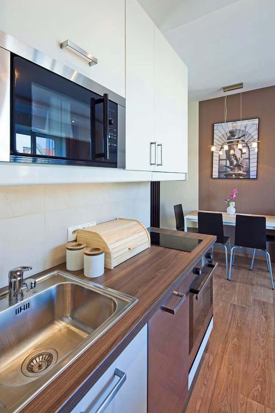 A sleek and compact kitchen area with white cabinets, a sink, and modern appliances. The open-plan layout connects to the dining space.