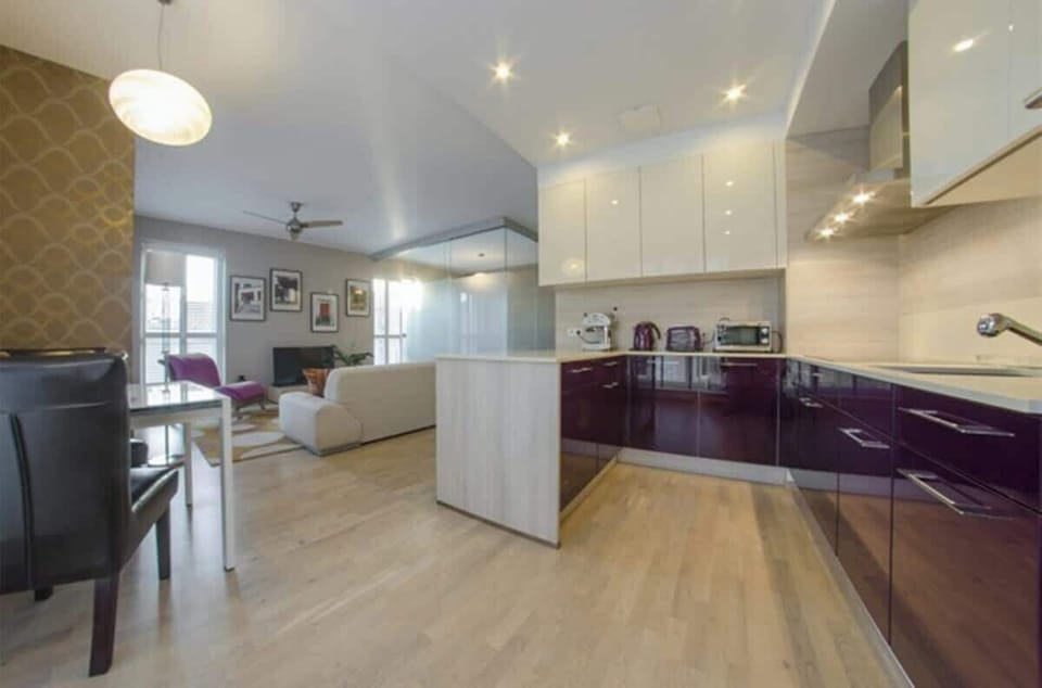 The fully equipped space offers high-quality appliances, such as a dishwasher, oven, coffee machine, hob, and fridge. Large windows illuminate the area, and the elegant dining table allows for meals to be enjoyed in a comfortable setting.