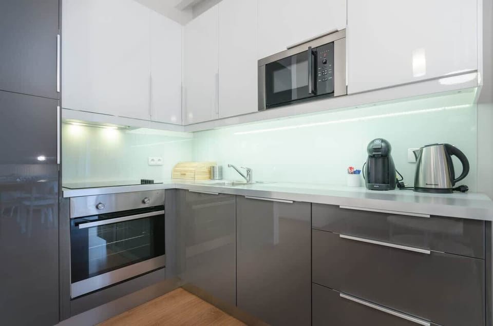 A modern kitchen designed in elegant, glossy grays with contrasting white accents. Equipped with high-quality appliances such as an oven, microwave, kettle, it ensures convenience and functionality.