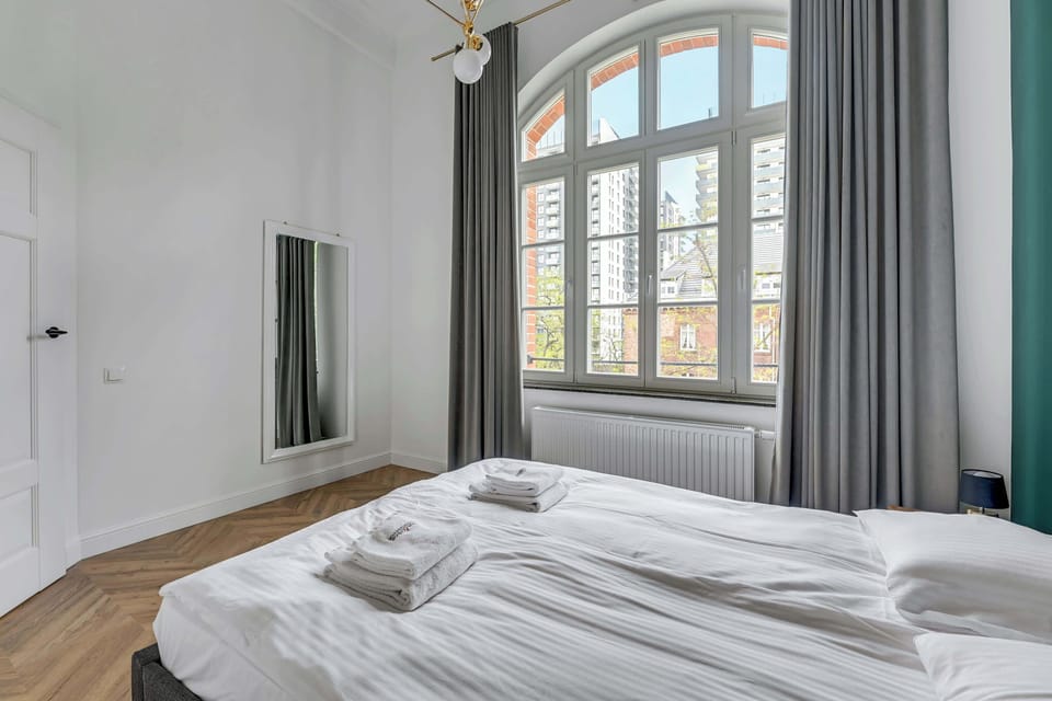 Another well-designed bedroom with a teal bed, large arched windows, and luxurious curtains framing the natural light.