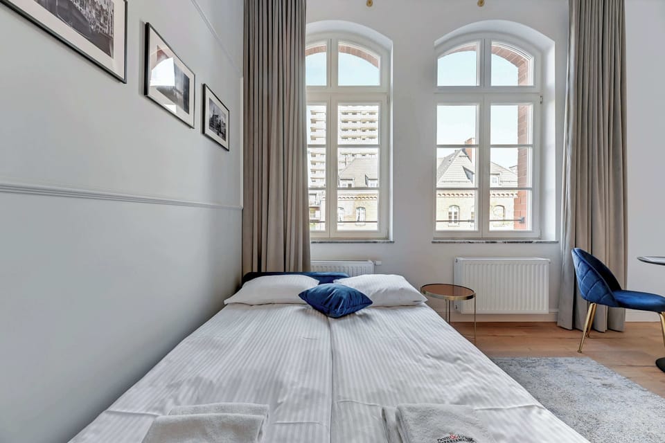 Another perspective of the studio, highlighting the blue sofa bed and the spacious, airy layout with arched windows.