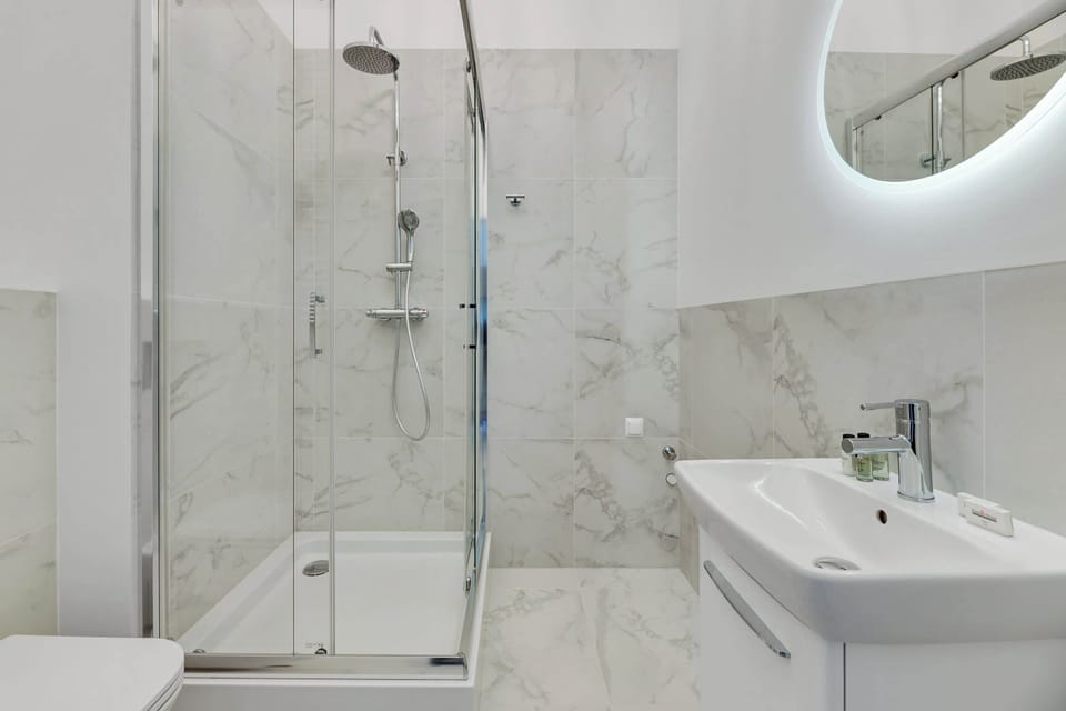 A stylish bathroom with marble-patterned tiles, a glass walk-in shower, and sleek white fixtures.