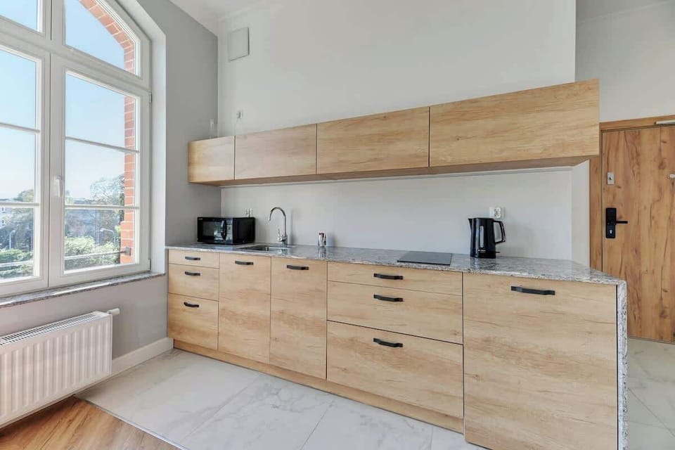 Sleek, modern charm with its natural wood cabinetry, clean lines, and minimalist design, enhanced by the light pouring in through the large windows, creating an inviting, airy ambiance.