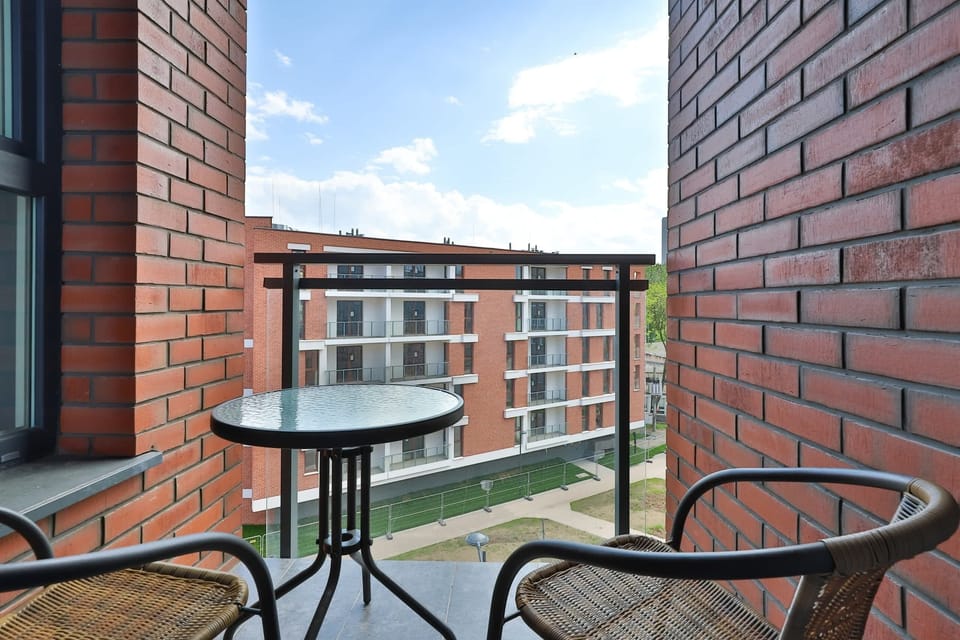 A cozy balcony setup with a round table and two chairs, overlooking a modern building facade and urban surroundings.